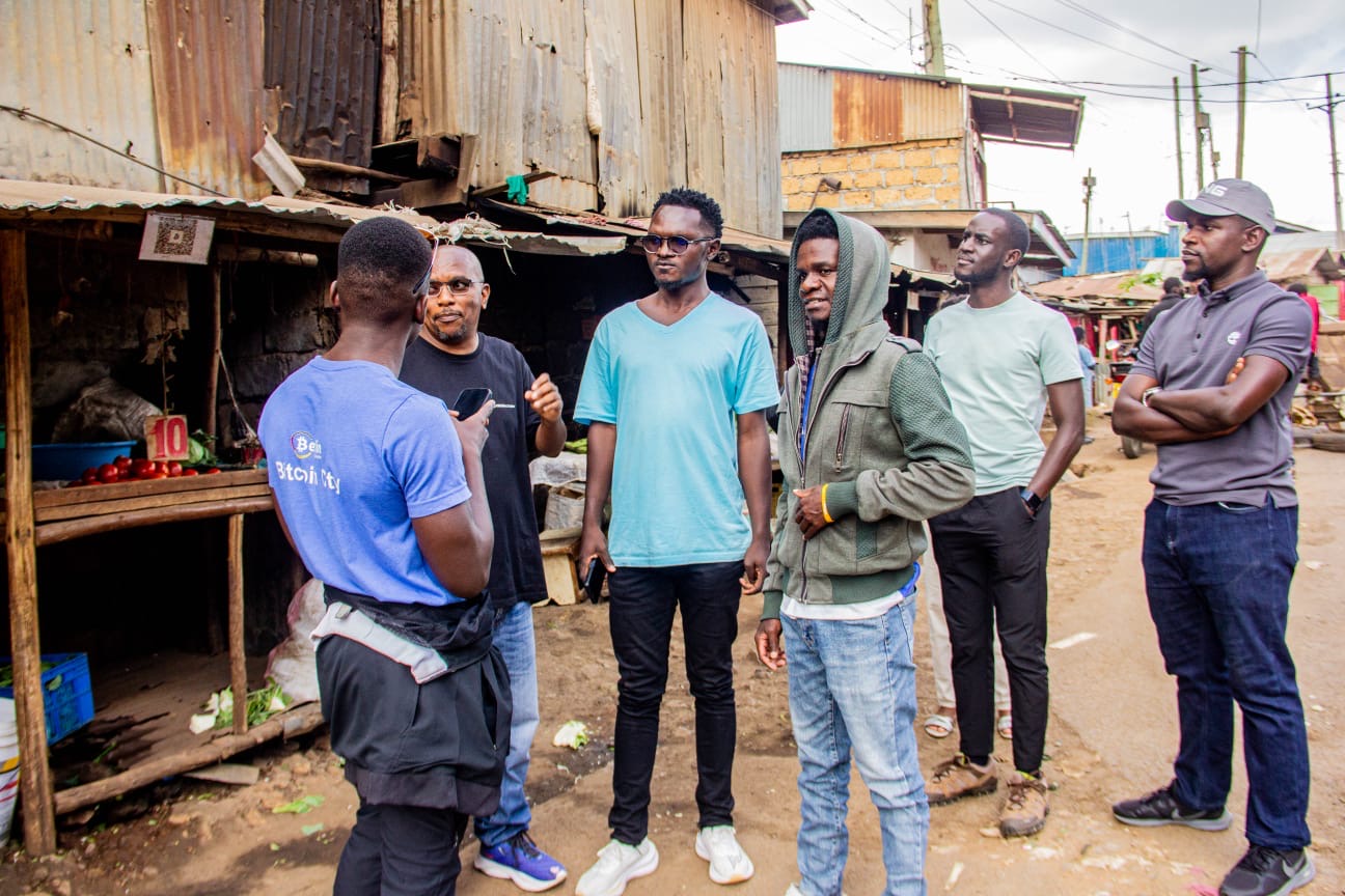 Brindon and the Afribit Kibera team at a vegetable stand in Bitcoin Valley, a Bitcoin QR code displayed on the stall