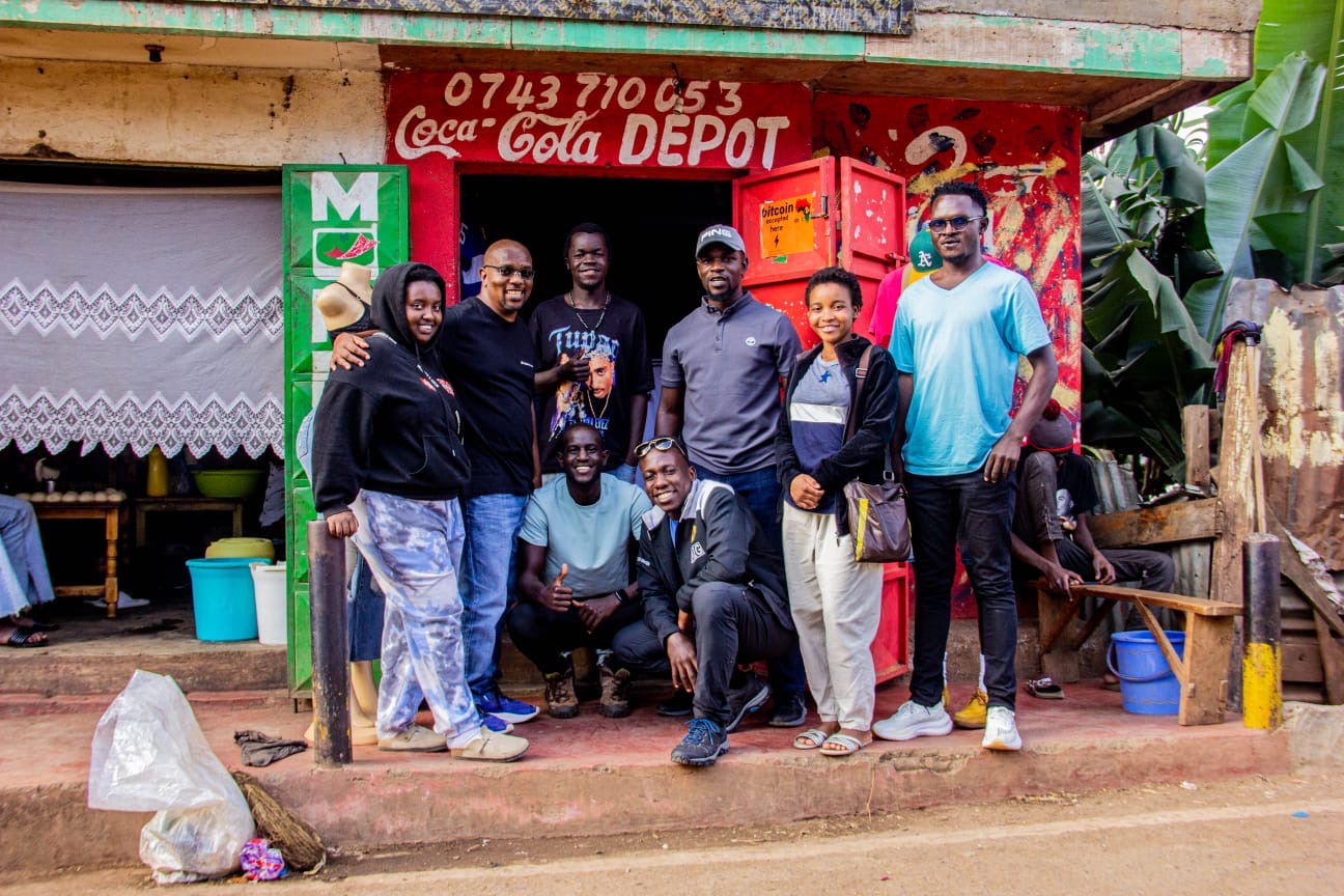 The group outside a Kibera general shop, a red fridge on the wall reading 'bitcoin accepted here'